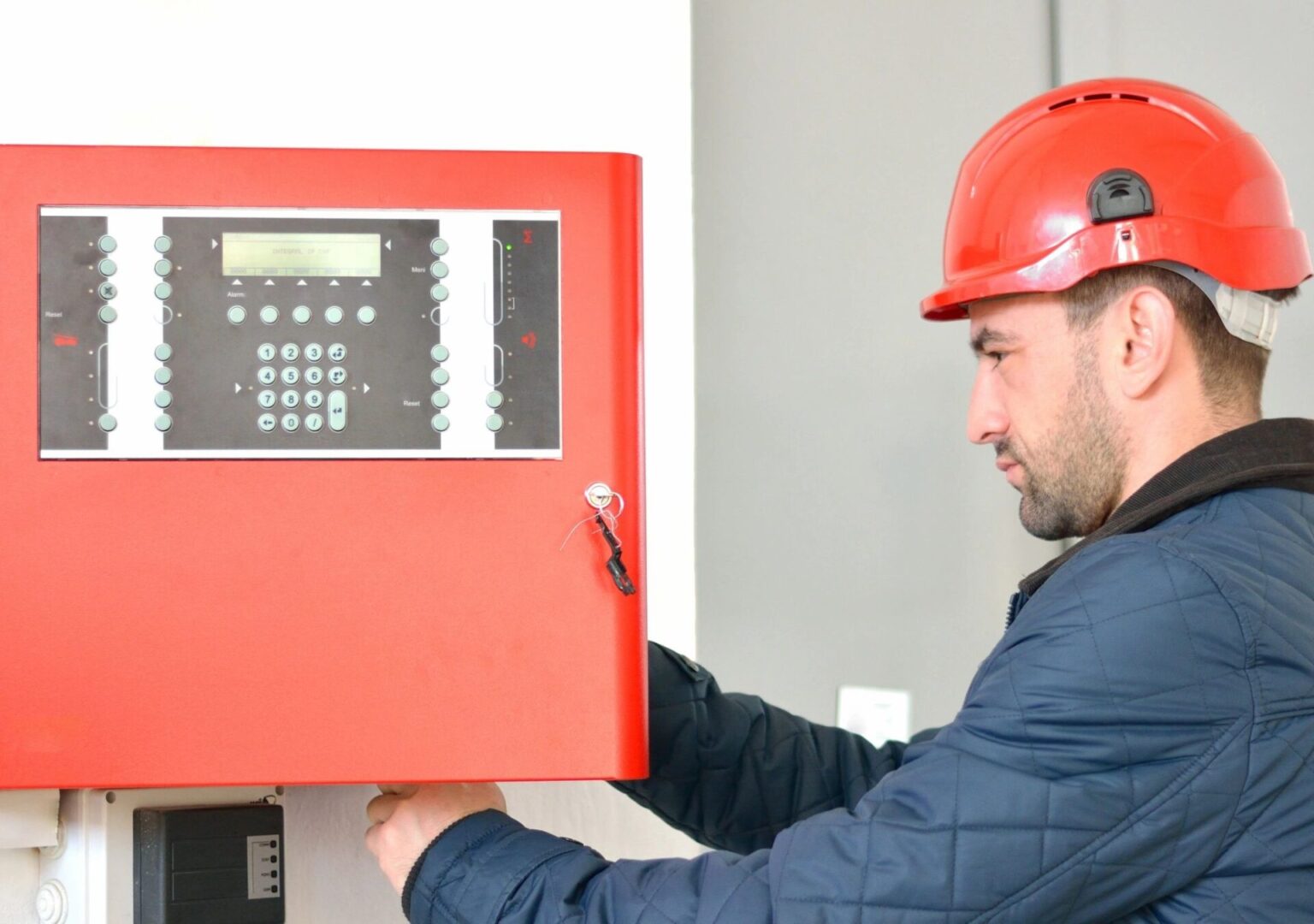 A man in a hard hat is working on a fire alarm.