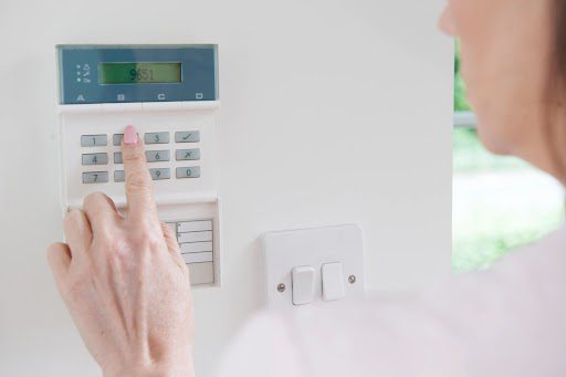 A woman pressing a button on a home security system.